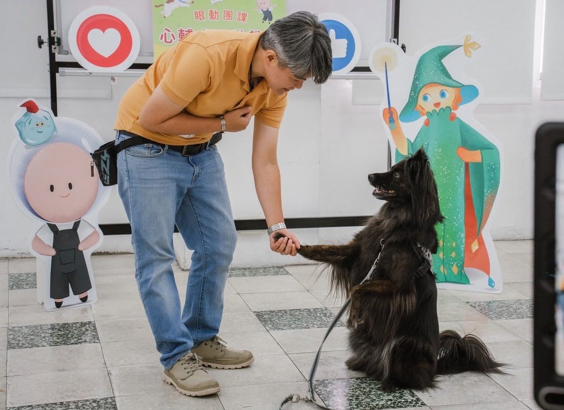 帶領人員在課程現場，與黑色長毛犬練習握手